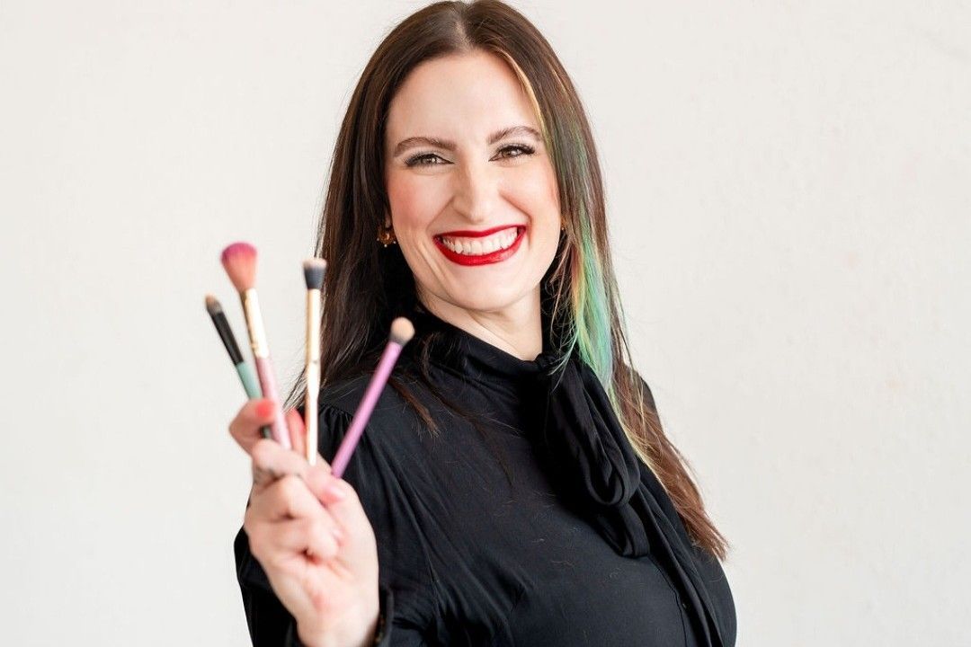 Monica Halligan makeup and brow specialist holding makeup brushes against a plain background